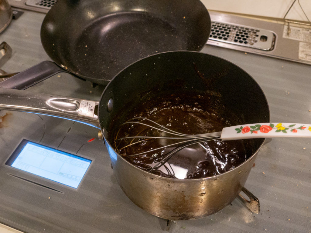 鍋に入れた砂糖と味噌と酒を、コンロのうえで、泡立て器で混ぜているところ